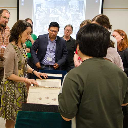 Participants gather around Daniela Bleichmar to look at archival materials
