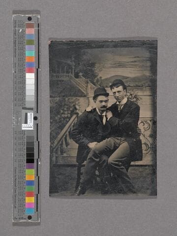 Two unidentified men in hats in front of painted mountain backdrop