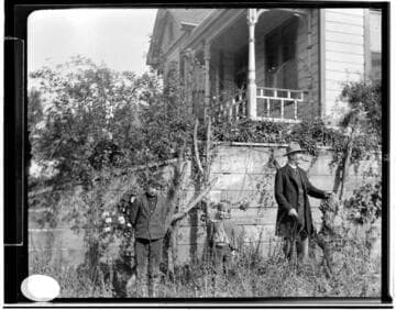 A man and two young boys standing by a wall below a residence