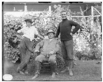 Three men posed in residential garden; the man seated is Ben Pearson