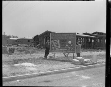Two men standing by Reddy Killowatt sign at home construction sites
