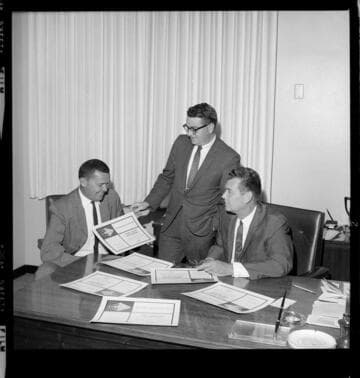 Three men at an office with award certificates