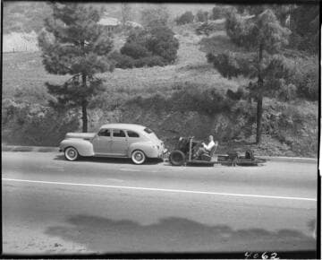 Man parking the 3 wheel vehicle without a body behind another car.  The single rear wheel is the one that turns