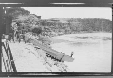 Men lowering one of the Colorado River Expedition boats down the bank to the Colorado River
