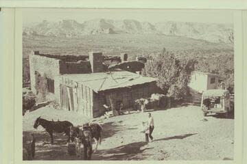 The burned Rainbow Lodge main building.  Ralph Cameron tends to the packing.  Octagon Butte at left in distance.  Cummings Mesa on horizon