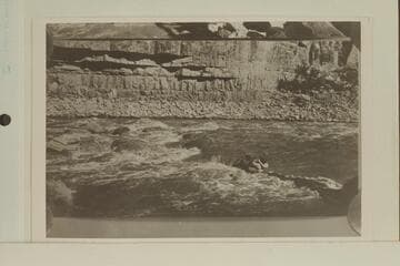 One of the Kolbs working out to the rock-locked boat in Dark Canyon Rapid.  USGS Cataract Canyon survey under W. R. Chenoweth.  Copy of small print loaned by Chenoweth.  "Emery Going Out," Lint album