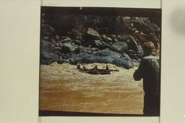 Georgie White's smaller inflated boats in Vulcan Rapid.  The two oarsmen seem to be struggling to maintain some sort of control while the passengers sit with backs toward the rapid