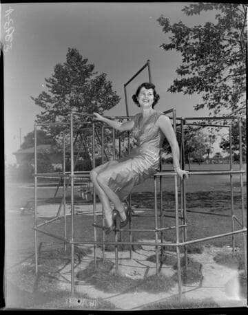 Young lady in a dress and high heals sitting in monkey bars at park playground