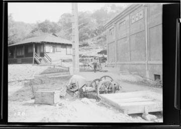 Exterior view of Kaweah #3 Power House and a cottage with a person in the foreground walking towards the camera and a broken wagon