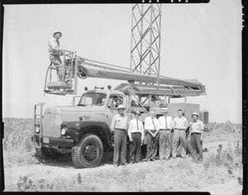 Group photo with linemen & supervisors and a boom truck near a transmission tower