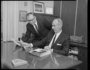 Execs. reviewing photographs and off-set portraits of both men