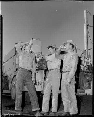 One lineman filling cup and two linemen drinking water from jug on back of line truck