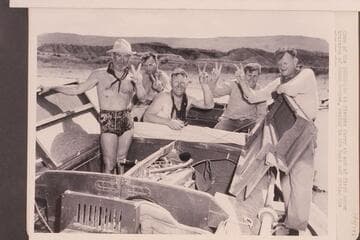 Crew of the "Esmeralda" at Pierces Ferry at end of first motor traverse of Grand Canyon, posing in the boat and giving the victory sign. Left to right: Marston, Robinson, Ed Hudson, Edward Hudson and Taylor
